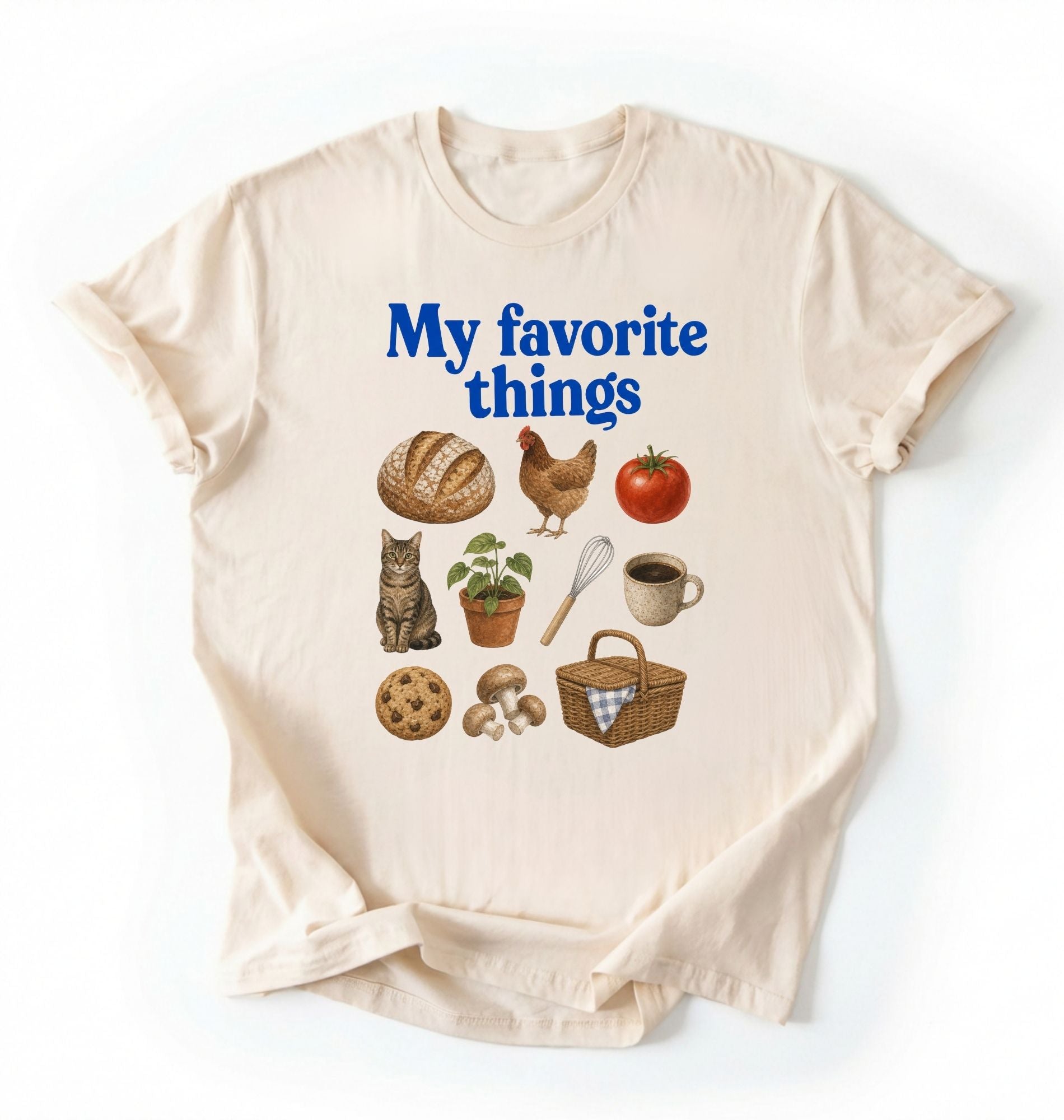 Flat lay of a cream my favorite things shirt with bread chicken coffee plants and cottagecore homestead illustrations on a white background