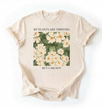 Flat lay of an ivory Gardener t-shirt with floral design and text my plants are thriving but i am not plant lover gift on a white background 