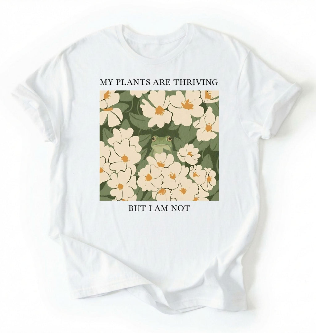 Flat lay of a white Gardener t-shirt with floral design and text my plants are thriving but i am not plant lover gift on a white background 
