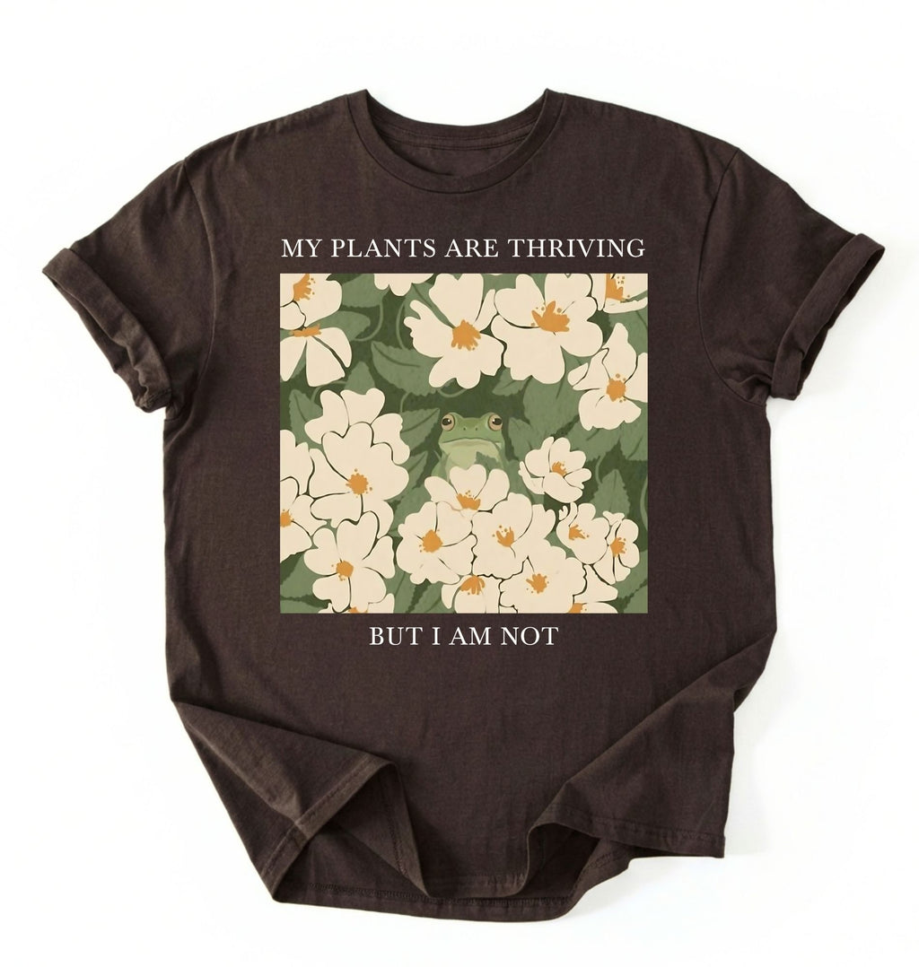 Flat lay of a dark_chocolate Gardener t-shirt with floral design and text my plants are thriving but i am not plant lover gift on a white background 