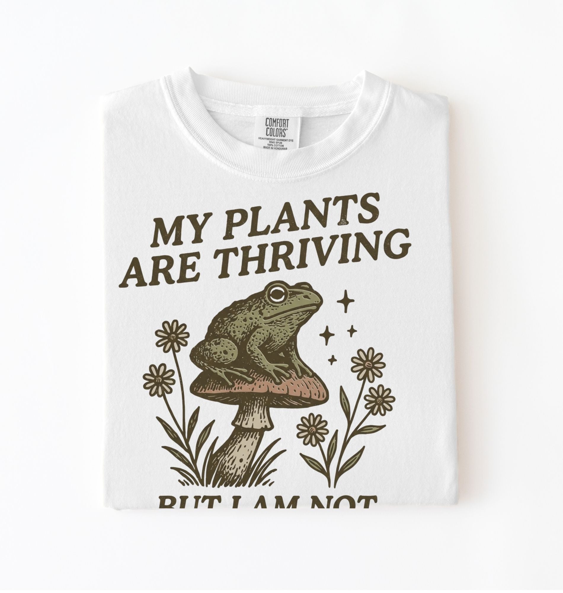white Comfort Colors sweatshirt with frog on mushroom illustration and text my plants are thriving but I am not
