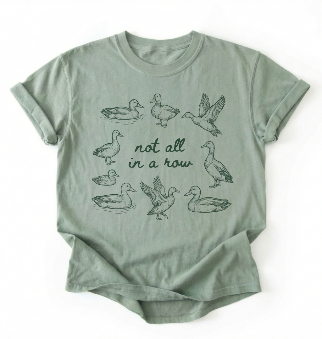Flat lay of an bay duck graphic t-shirt with hand drawn ducks and not all in a row text, funny animal shirt gift on a white background 