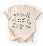 Flat lay of an Ivory duck graphic t-shirt with hand drawn ducks and not all in a row text, funny animal shirt gift on a white background 