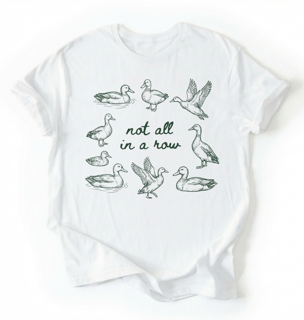 Flat lay of an bay duck graphic t-shirt with hand drawn ducks and not all in a row text, funny animal shirt gift on a white background 