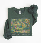 Flat lay of a forest green crewneck sweatshirt on a white background, featuring an impressionist floral garden artwork and white text reading “Now you’re just some garden that I used to hoe.