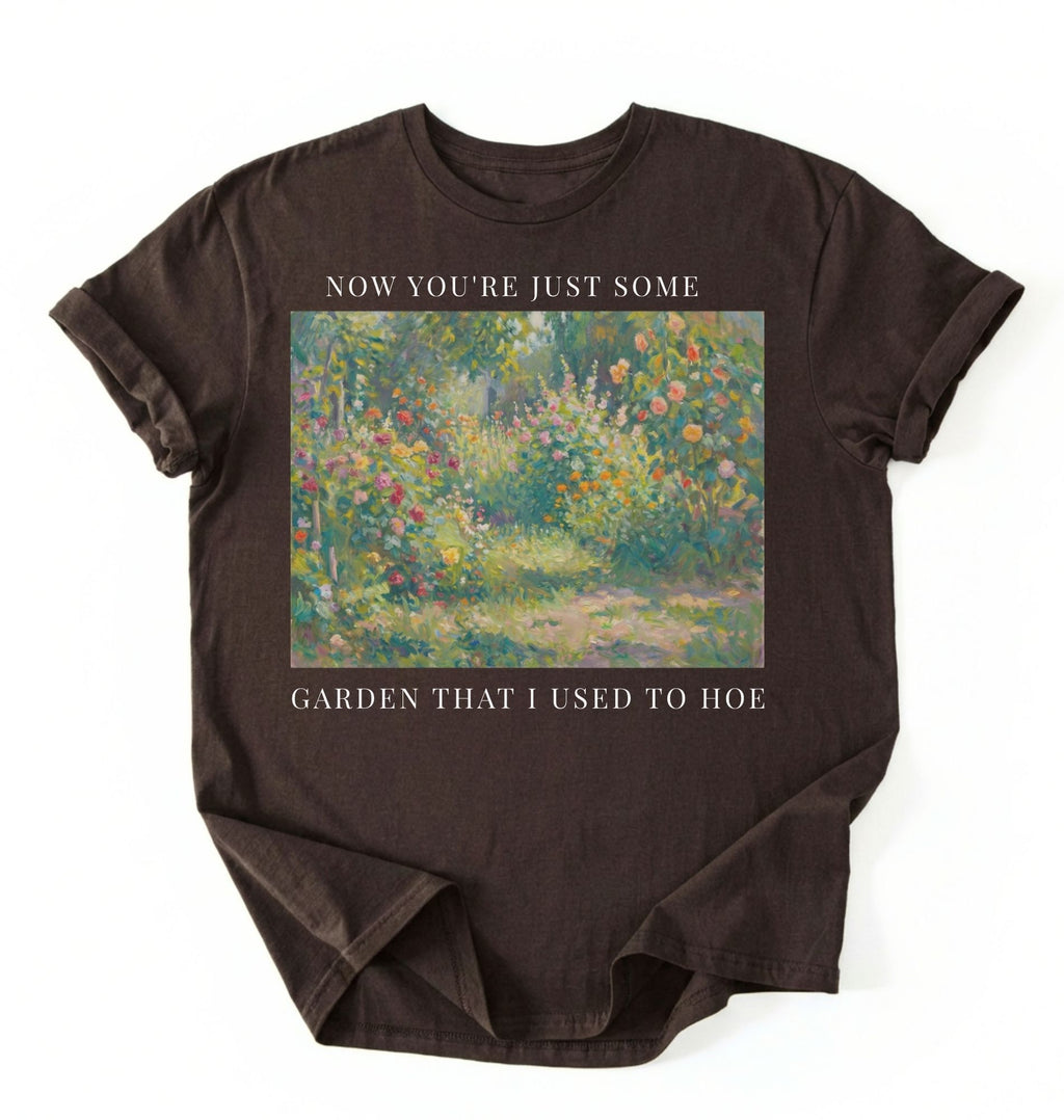 Flat lay of a dark chocolate shirt written Now you’re just some garden t-shirt with funny gardening pun, perfect gardener gift on a white background 
