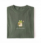Flat lay of a green sourdough shirt featuring a frog baker and the phrase Off to Feed My Starter on a white background
