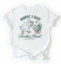 Flat lay white t-shirt with a graphic of a duck holding a plant and text 'Oops! I got another plant!' on a white background