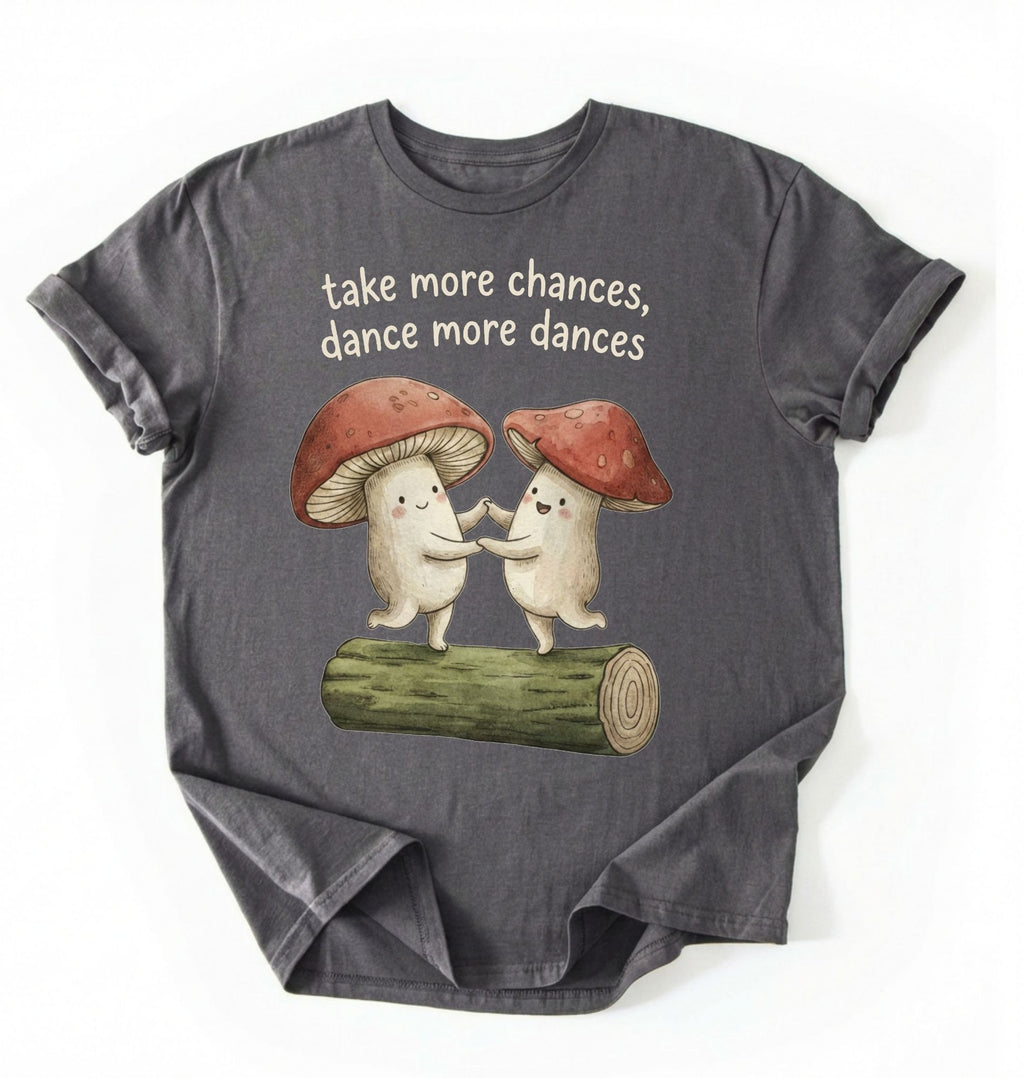 Flat lay of a Pepper charcoal t-shirt with two dancing mushrooms and the phrase take more chances dance more dances, whimsical cottagecore gift tee on a white background 