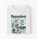 Flat lay of a white t-shirt featuring a botanical diagram with text reading “Photosynthesis Power Up.” for plant lovers and science fans perfect gardening gift for biology teachers and nature enthusiasts on a white background  