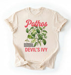 Flat lay of a natural t-shirt featuring a botanical leaf illustration of Pothos leaves with text reading “Pothos Devil’s Ivy” perfect gift for plant lovers and houseplant enthusiasts on white background 