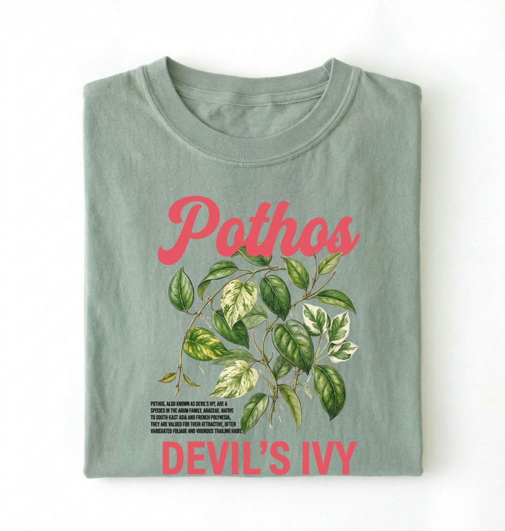 Flat lay of a bay t-shirt featuring a botanical leaf illustration of Pothos leaves with text reading “Pothos Devil’s Ivy” perfect gift for plant lovers and houseplant enthusiasts on white background 