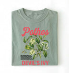 Flat lay of a bay t-shirt featuring a botanical leaf illustration of Pothos leaves with text reading “Pothos Devil’s Ivy” perfect gift for plant lovers and houseplant enthusiasts on white background 
