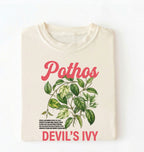Flat lay of a ivory t-shirt featuring a botanical leaf illustration of Pothos leaves with text reading “Pothos Devil’s Ivy” perfect gift for plant lovers and houseplant enthusiasts on white background 