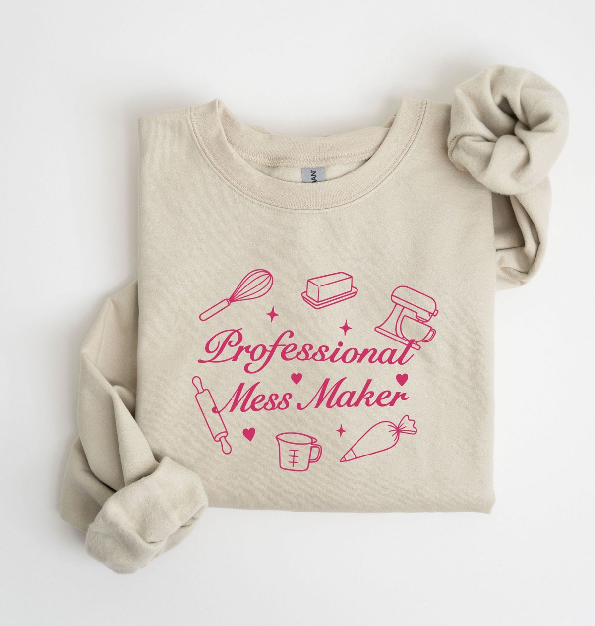 A beige crewneck sweatshirt with rolled sleeves, featuring a pink graphic print that reads 'Professional Mess Maker' surrounded by baking and kitchen utensil illustrations, laid flat on a white background.