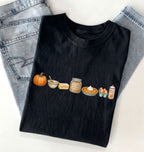 Flat lay of a Black fall baking shirt featuring a pumpkin, mixing bowl, butter, brown sugar, pumpkin pie, eggs and whipped cream on a white background 