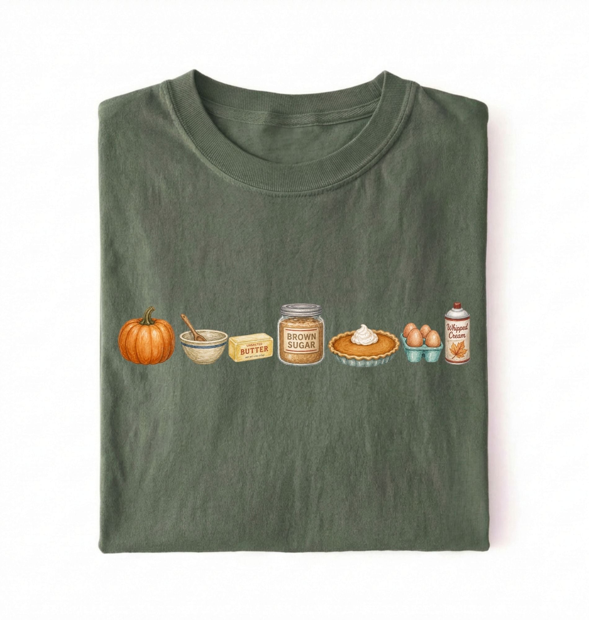 An olive green folded t-shirt with a horizontal graphic print of autumn baking ingredients, including a pumpkin, butter, brown sugar, pie, eggs, and whipped cream, on a white background.