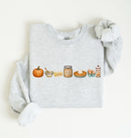 A light heather gray long-sleeve sweatshirt with a watercolor-style autumn baking graphic on the chest, featuring a pumpkin, bowl, butter, sugar, pie, eggs, and spices. The sweatshirt is styled flat on a warm off-white background with one sleeve rolled up.