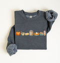 A dark heather gray crewneck sweatshirt with rolled cuffs, featuring a colorful graphic print of autumn baking ingredients (pumpkin, butter, honey, pie, eggs, syrup) across the chest, laid flat on a light cream background.