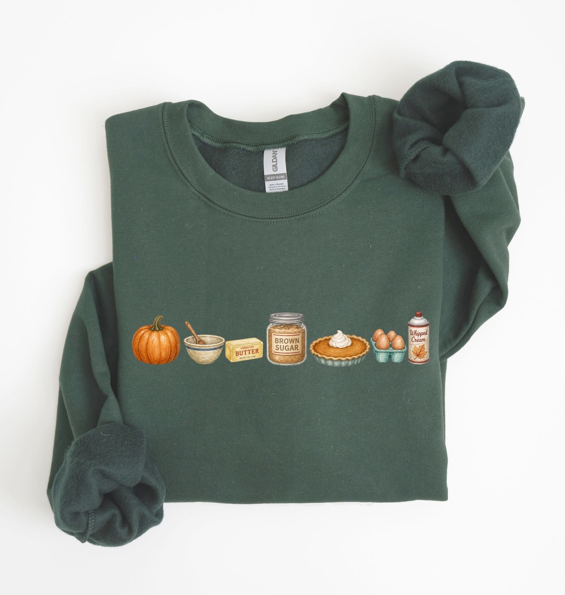 A dark green crewneck sweatshirt with a horizontal graphic print of autumn-themed items including a pumpkin, butter, honey, pie, eggs, and whipped cream. The sweatshirt is styled flat on a white background with rolled cuffs.