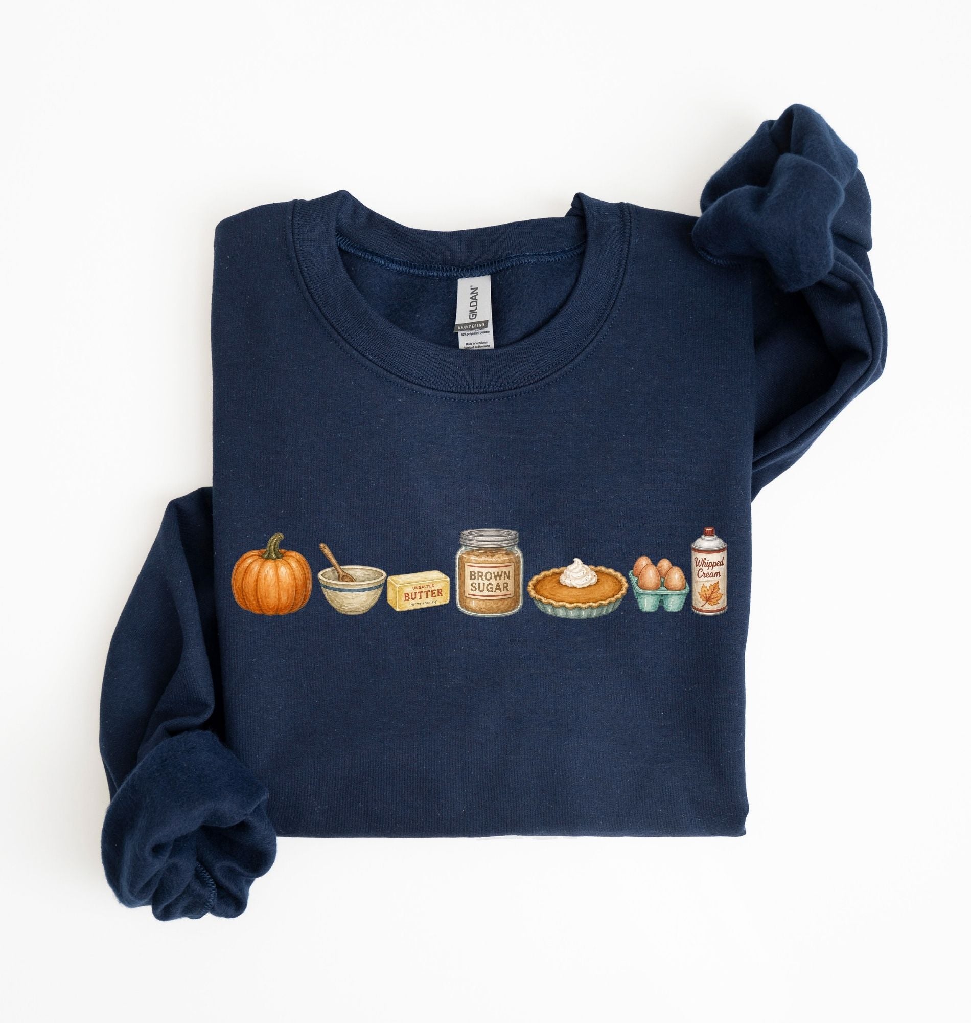 Flat lay of a navy blue Gildan sweatshirt featuring a pumpkin, mixing bowl, butter, brown sugar, pumpkin pie, eggs and whipped cream on a white background 