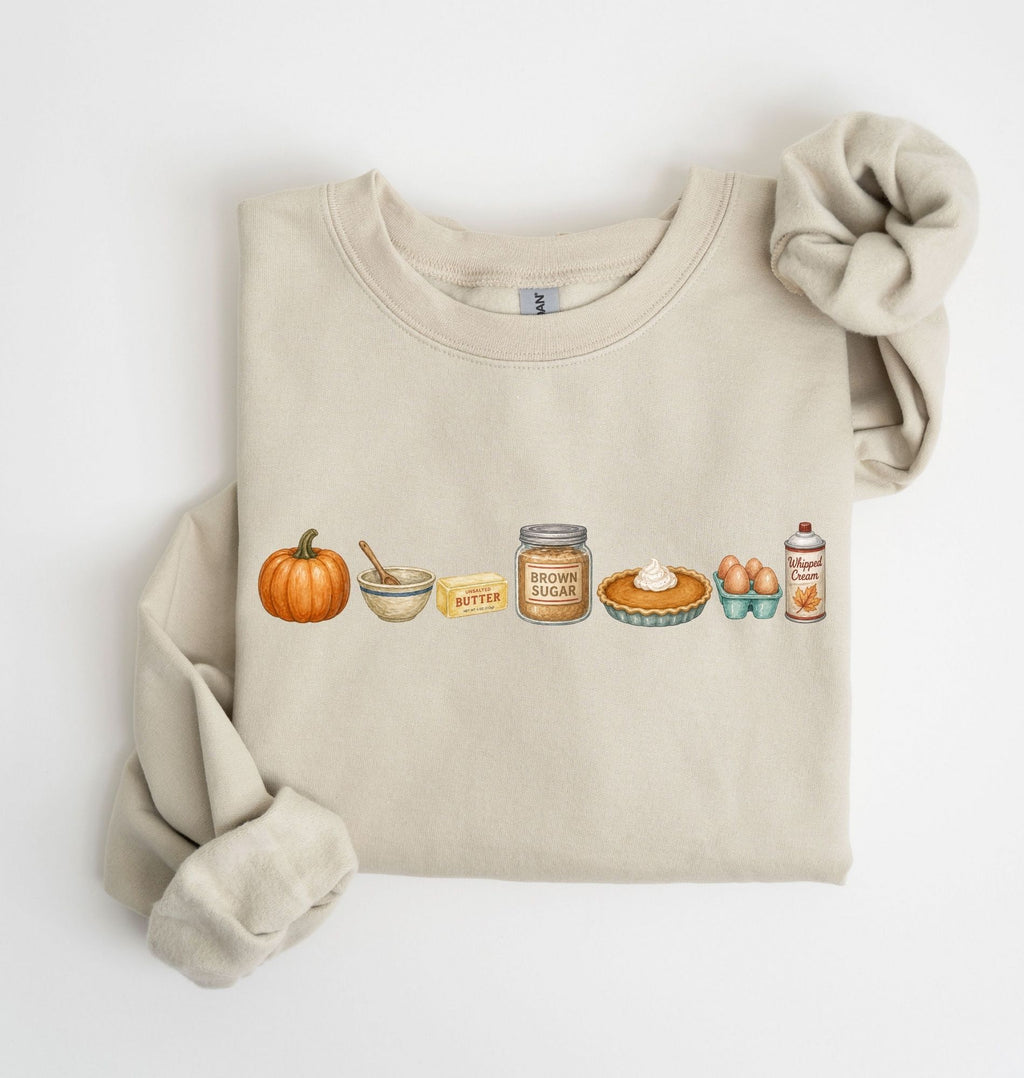 Flat lay of a sand blue Gildan sweatshirt featuring a pumpkin, mixing bowl, butter, brown sugar, pumpkin pie, eggs and whipped cream on a white background 