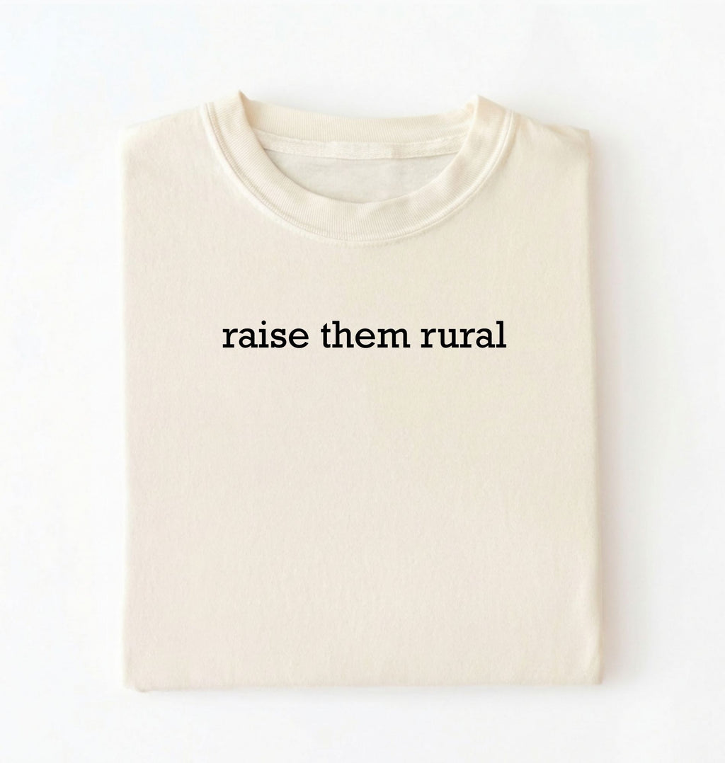 Flat lay of a Raise Them Rural country graphic shirt in ivory for farm families rural lifestyle and country living on a white background