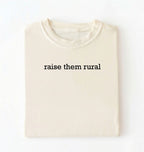 Flat lay of a Raise Them Rural country graphic shirt in ivory for farm families rural lifestyle and country living on a white background