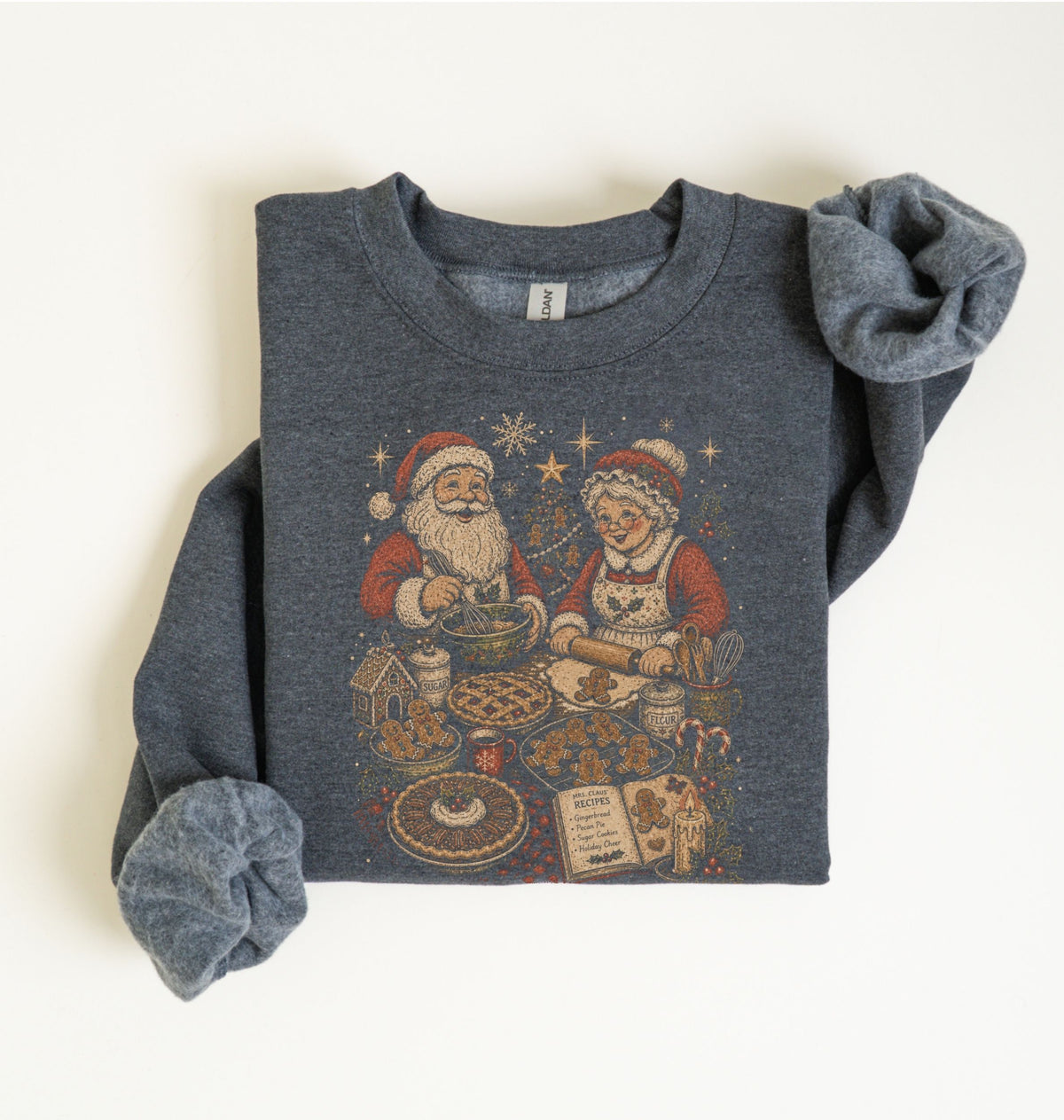 A folded dark heather gray sweatshirt with rolled sleeves, featuring a vintage-style Christmas graphic of Santa Claus and a woman baking cookies. The sweatshirt is laid flat on a light cream background.
