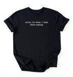 A folded black-colored t-shirt with black typewriter-style text reading 'Sorry for What I Said While Baking' on the front, displayed against a clean white background.