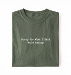 A folded green t-shirt with the black printed text 'Sorry for What I Said While Baking' centered on the chest, presented on a clean white background.