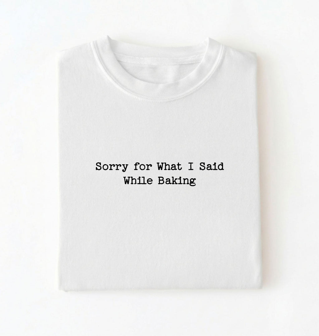 A folded white t-shirt with the black printed text 'Sorry for What I Said While Baking' centered on the chest, presented on a clean white background.