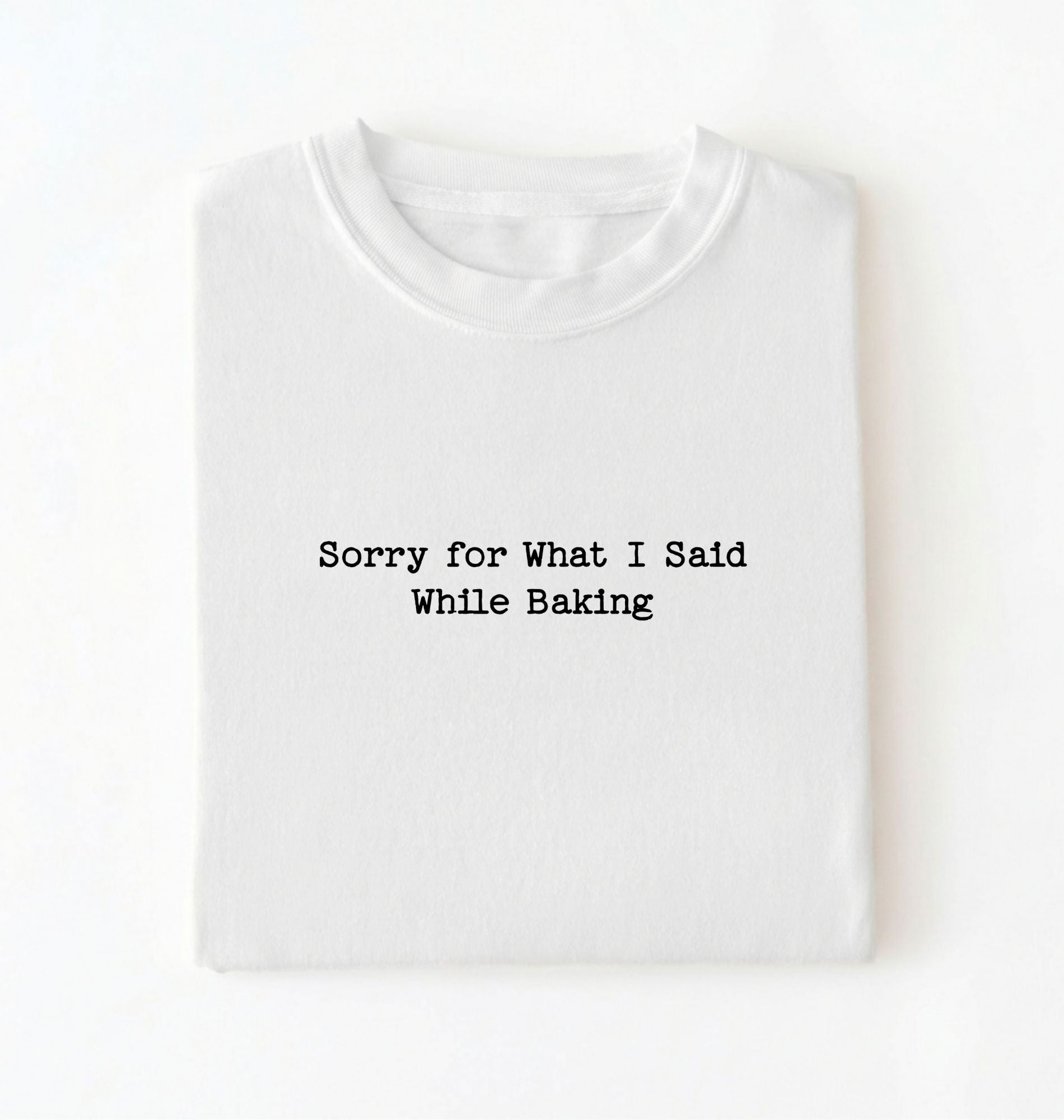 A folded white t-shirt with the black printed text 'Sorry for What I Said While Baking' centered on the chest, presented on a clean white background.