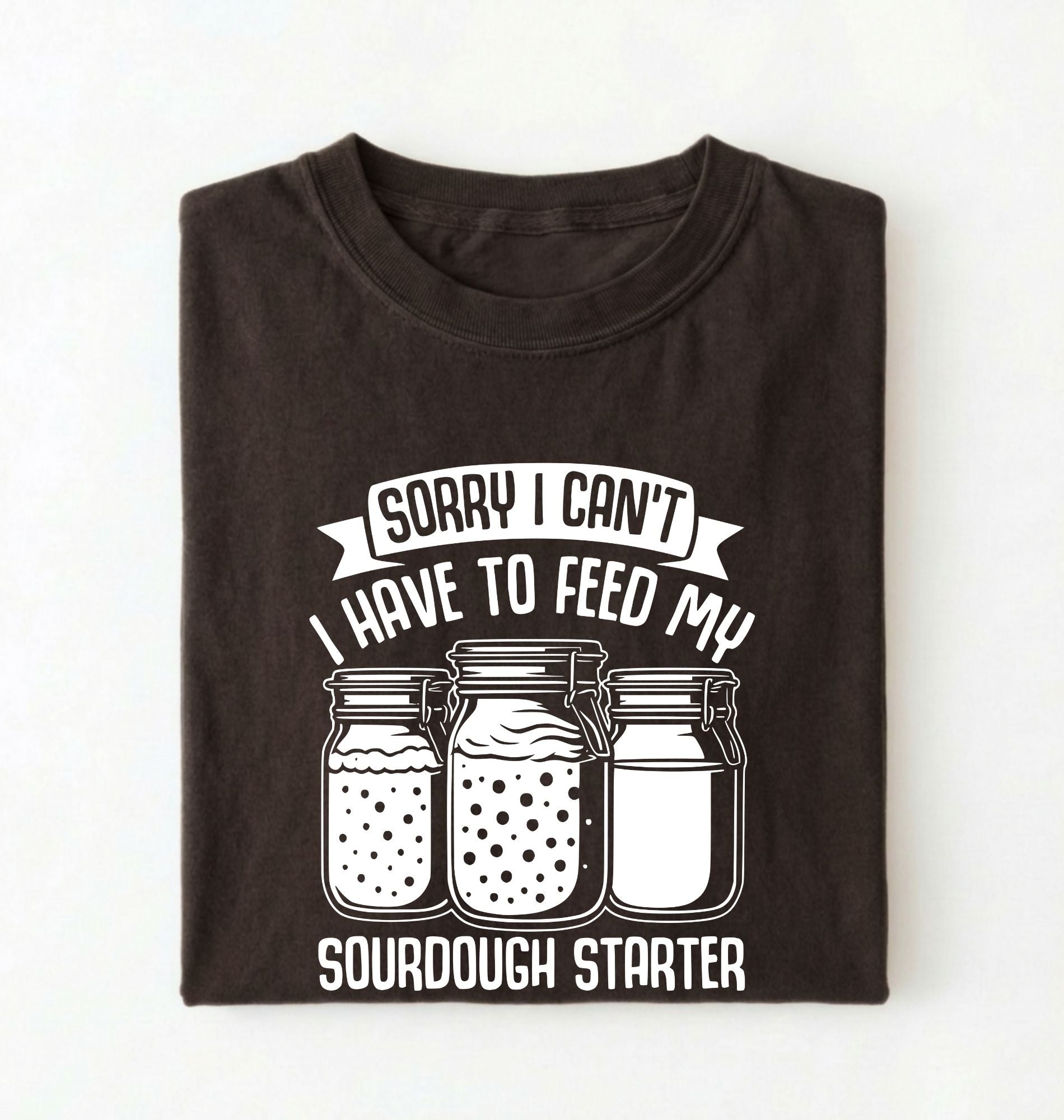 Flat lay of a brown Sorry I Can't I Have to Feed My Sourdough Starter shirt with starter jar graphic on charcoal t-shirt on a white background 