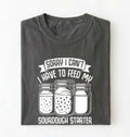 Flat lay of a pepper Sorry I Can't I Have to Feed My Sourdough Starter shirt with starter jar graphic on charcoal t-shirt on a white background 