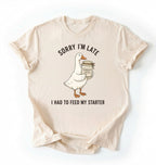 Flat lay of a natural sorry im late i had to feed my starter shirt with goose and sourdough starter jar funny baker gift on a white background