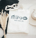 White tote bag with bread-making ingredients illustration and text on a textured surface.