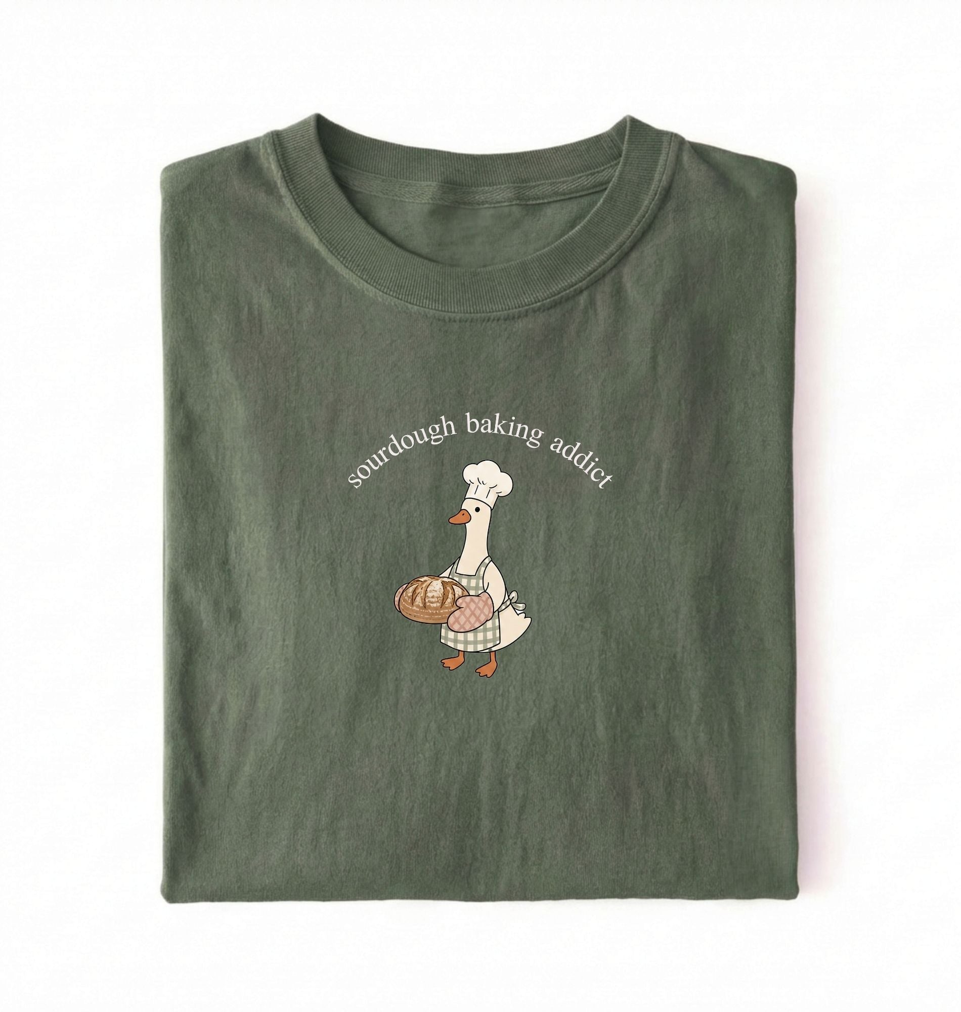Flat lay of a green Sourdough Baking Addict shirt with baker goose holding artisan bread for sourdough enthusiasts on a white background 