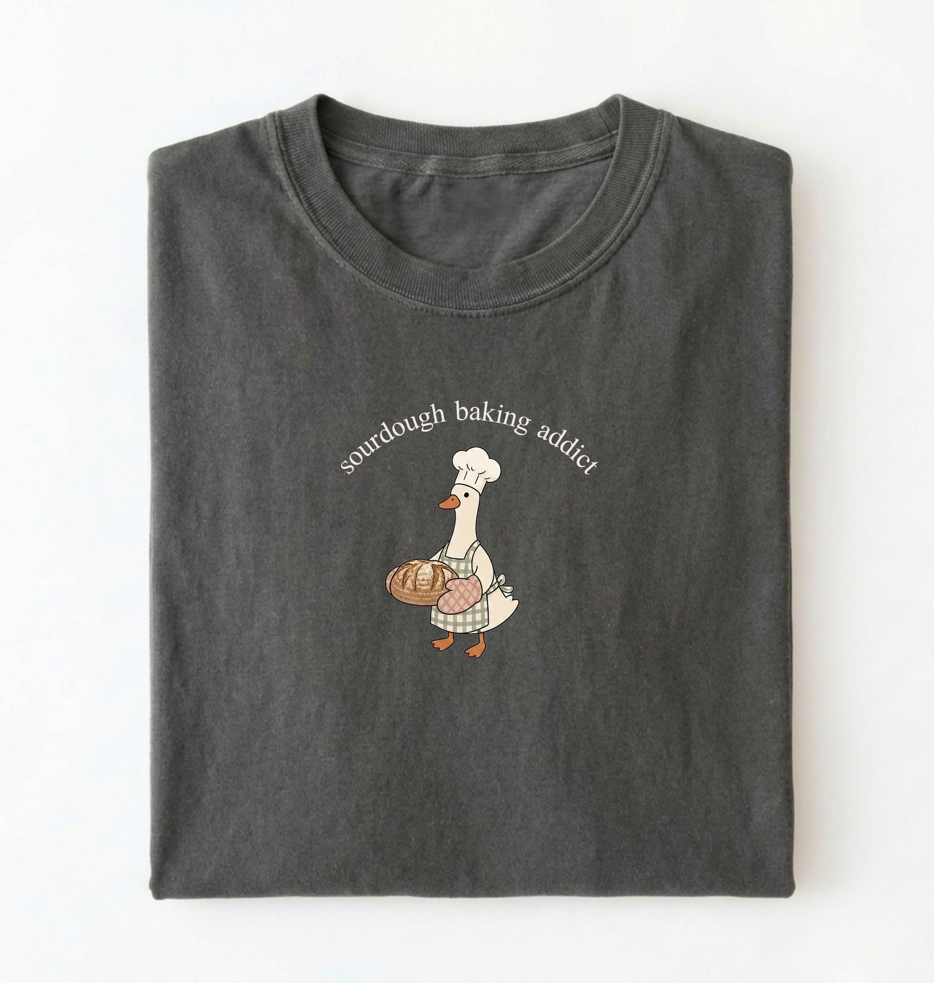 Flat lay of a dark grey Sourdough Baking Addict shirt with baker goose holding artisan bread for sourdough enthusiasts on a white background 
