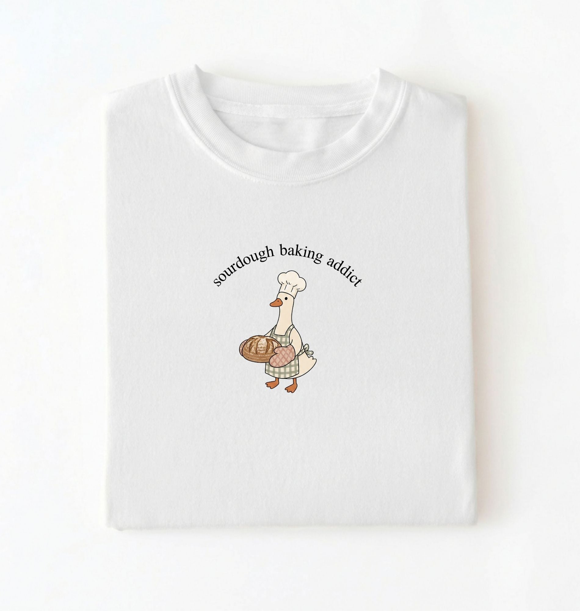 Flat lay of a white Sourdough Baking Addict shirt with baker goose holding artisan bread for sourdough enthusiasts on a white background 