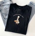 Black t-shirt with a graphic of a duck wearing a chef's hat and sourdough bread, text 'sourdough baking addict', on a light gray background.