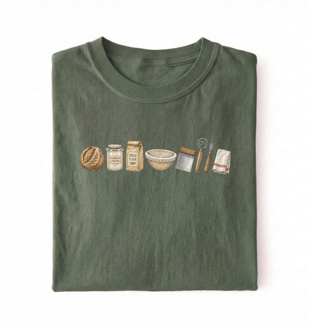 Flat lay of a green sourdough baking essentials shirt with starter flour dough bowl and bread making tools on a white background 
