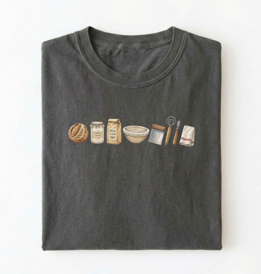 Flat lay of a charcoal sourdough baking essentials shirt with starter flour dough bowl and bread making tools on a white background 