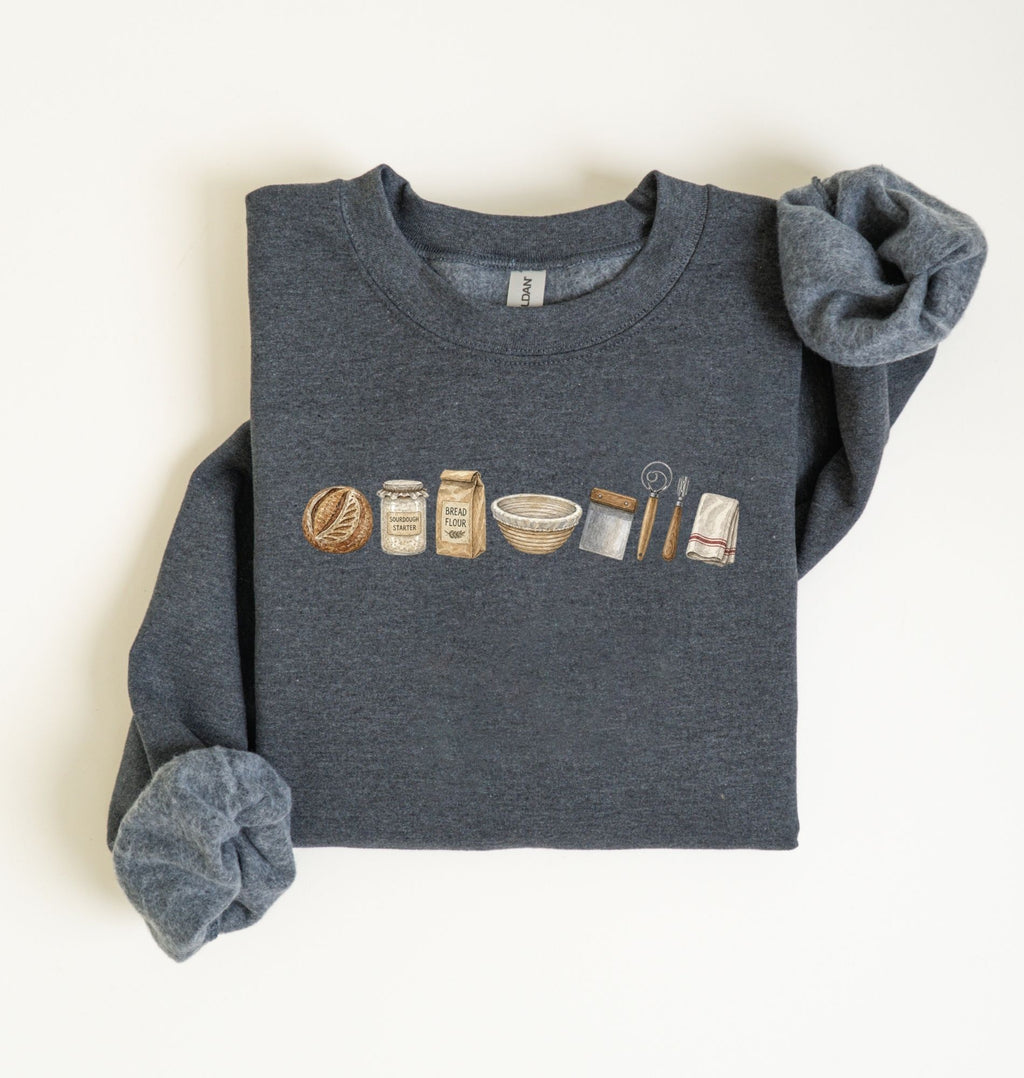 Flat lay of a dark heather sourdough baking essentials sweatshirt with bread starter flour bowl and baking tools on a white background 