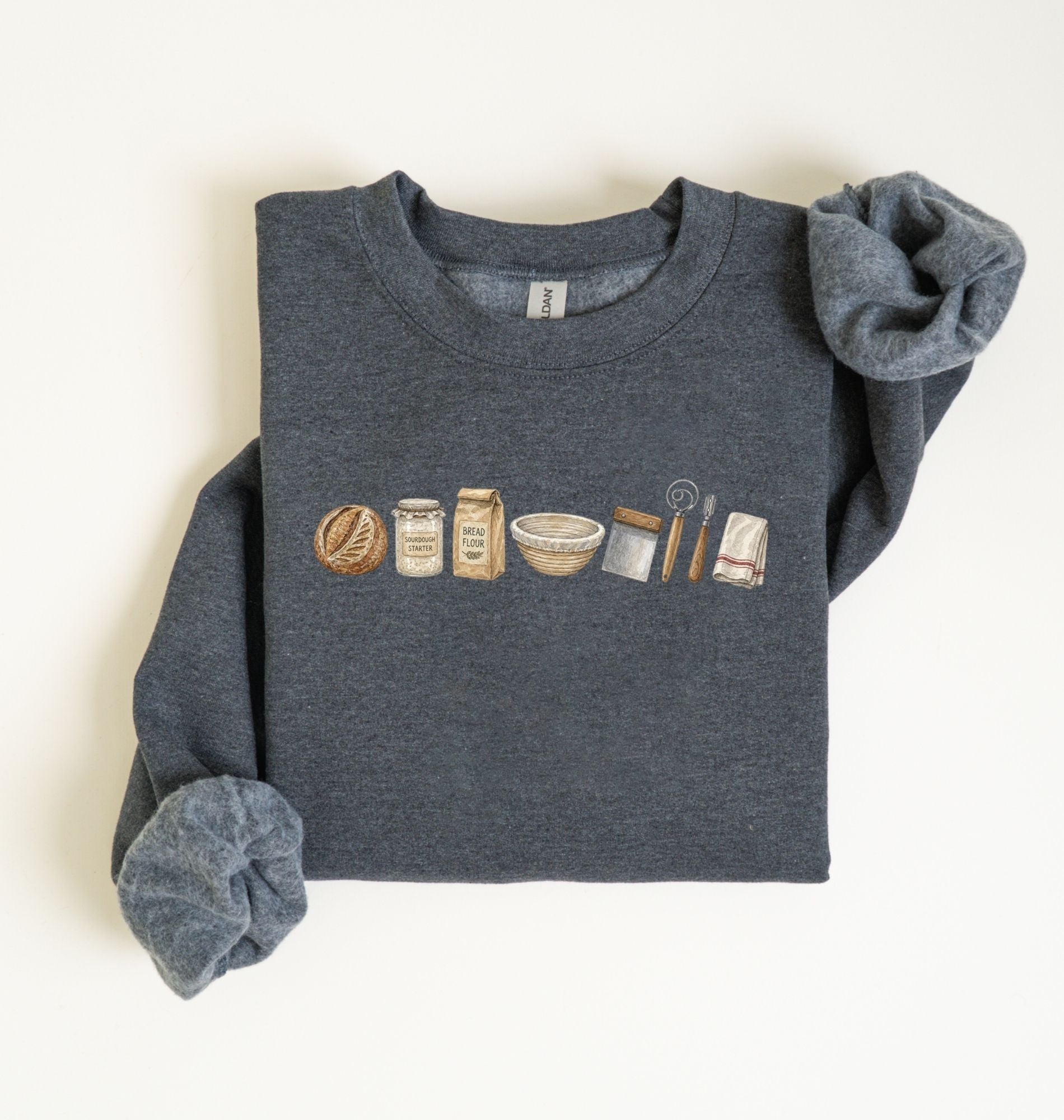 Flat lay of a dark heather sourdough baking essentials sweatshirt with bread starter flour bowl and baking tools on a white background 