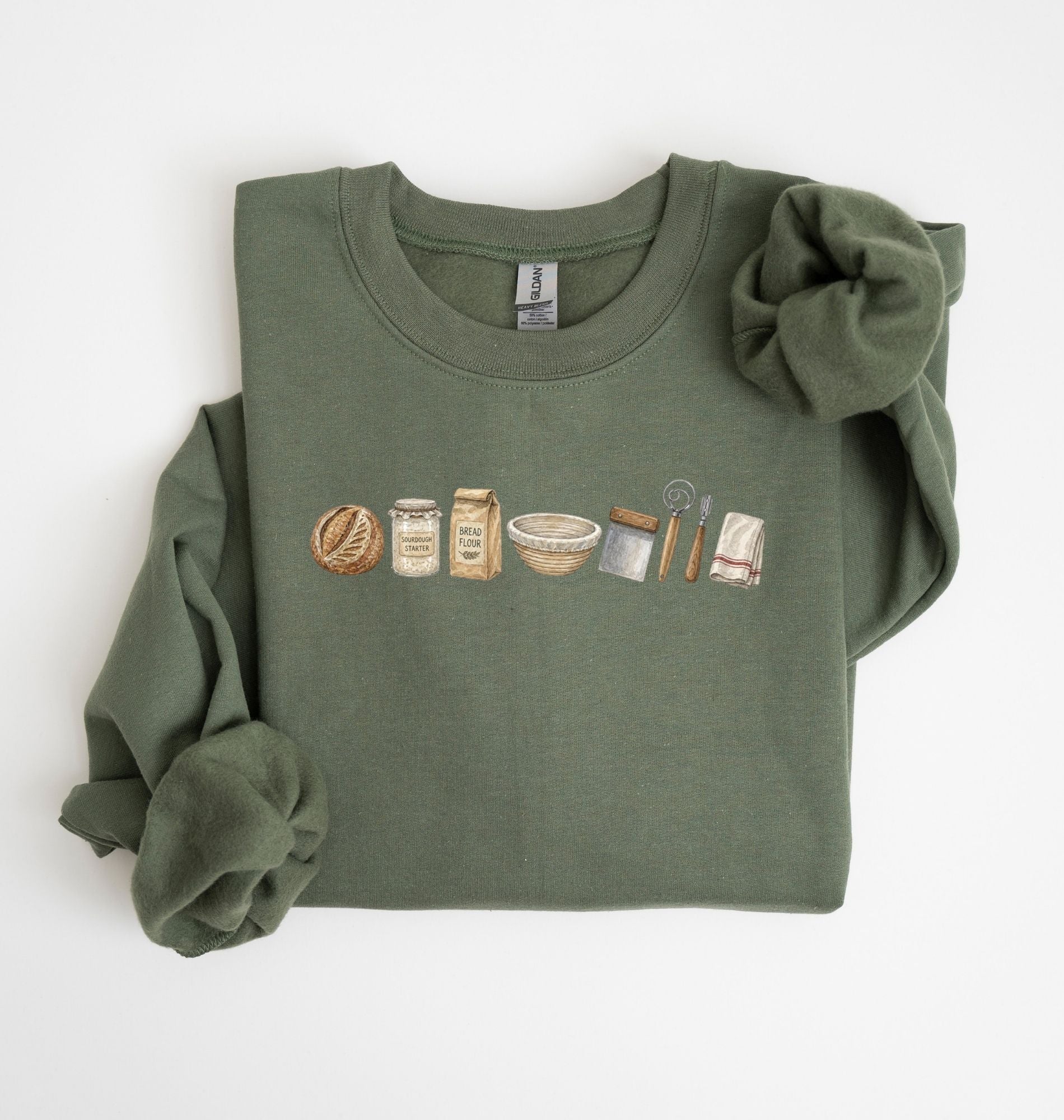Flat lay of a green sourdough baking essentials sweatshirt with bread starter flour bowl and baking tools on a white background 