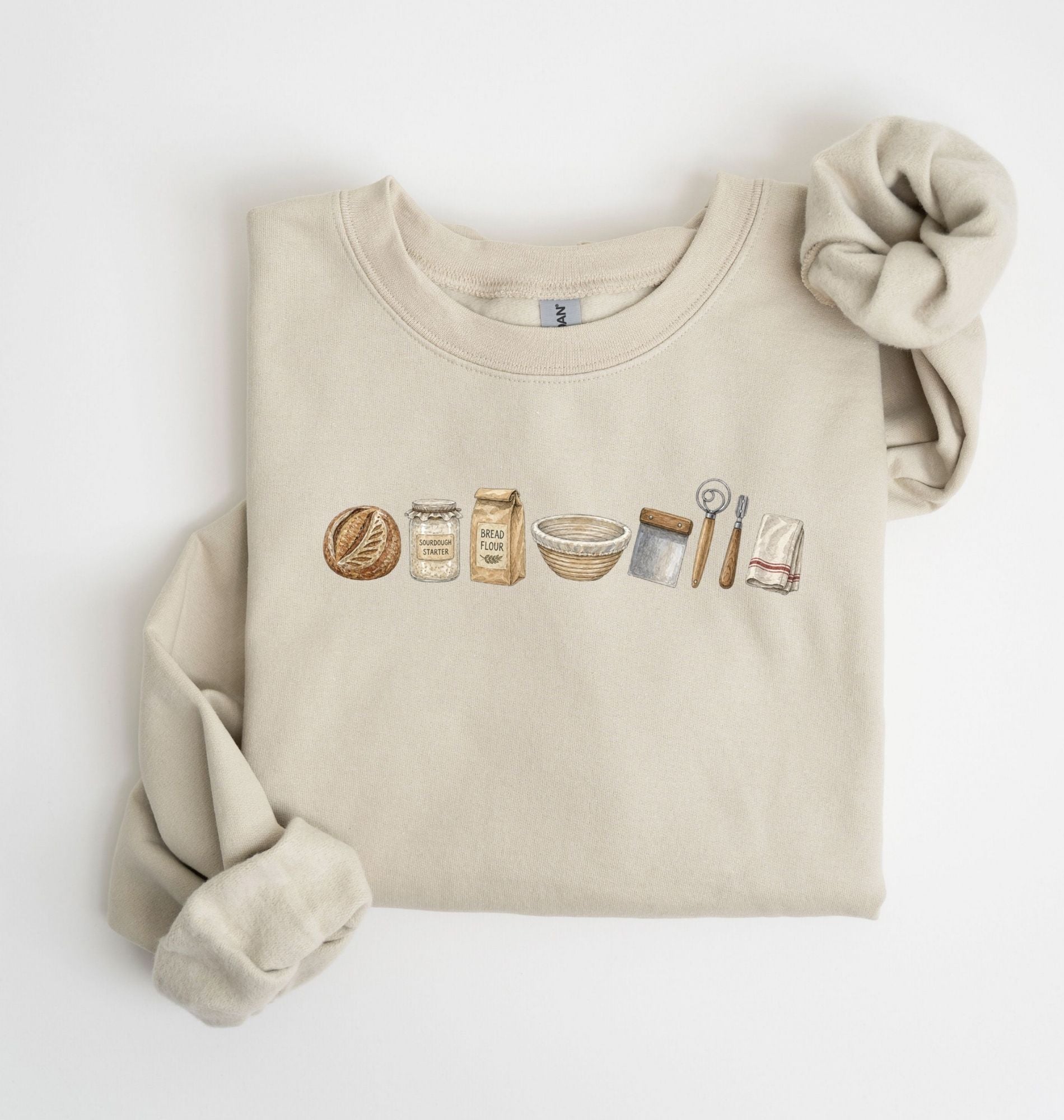 Flat lay of a sand sourdough baking essentials sweatshirt with bread starter flour bowl and baking tools on a white background 