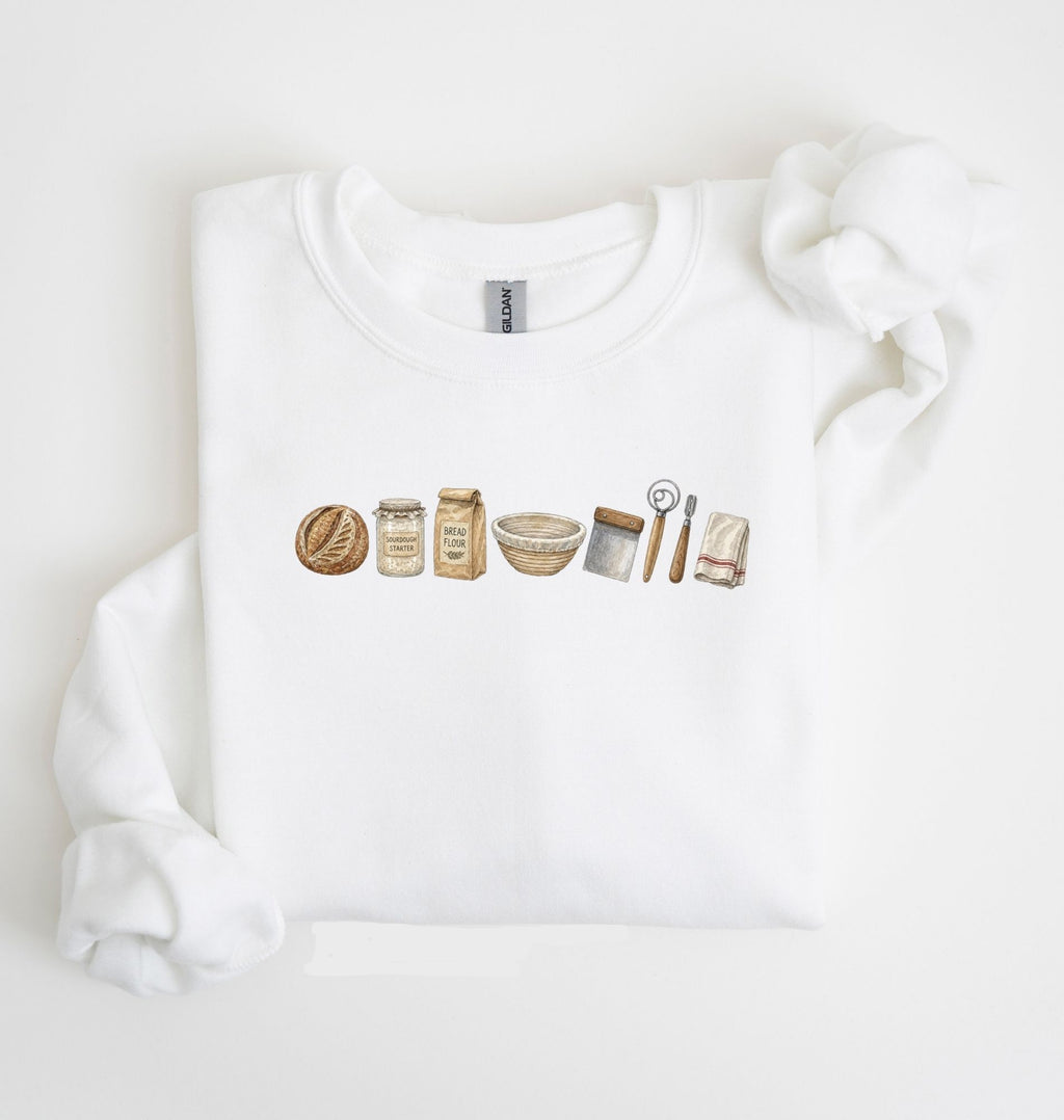 Flat lay of a white sourdough baking essentials sweatshirt with bread starter flour bowl and baking tools on a white background 