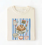 Flat lay of a cream Sourdough baking tools shirt featuring artisan bread, starter jar, banneton, and baking supplies on a white background 