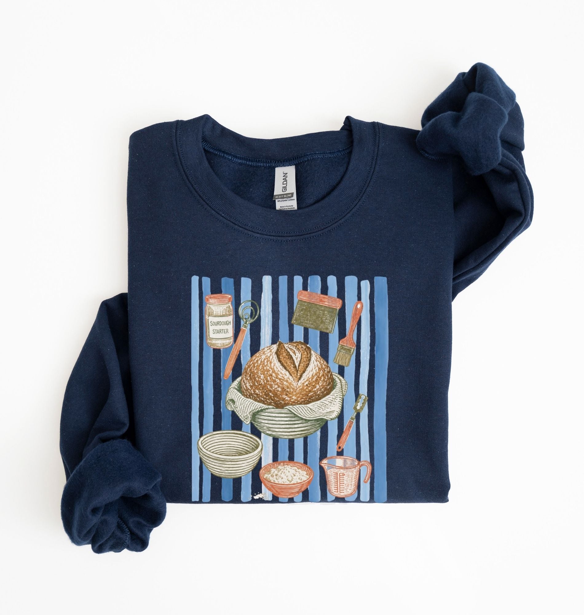 Flat lay of a navy blue Sourdough baking tools sweatshirt featuring artisan bread, starter jar, banneton, and baking supplies on a white background 